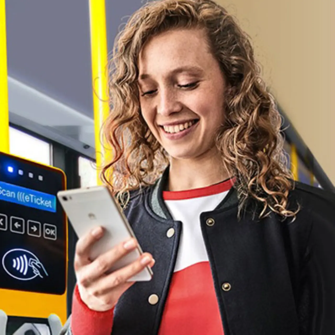 A woman is standing on a bus next to a contactless ticket machine, looking at her smartphone.