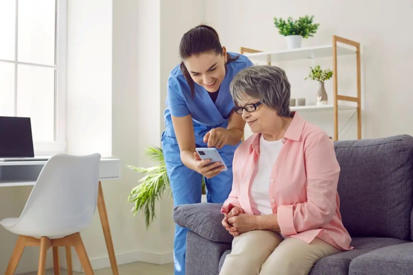 Female nurse shows elderly woman how to use mobile health application