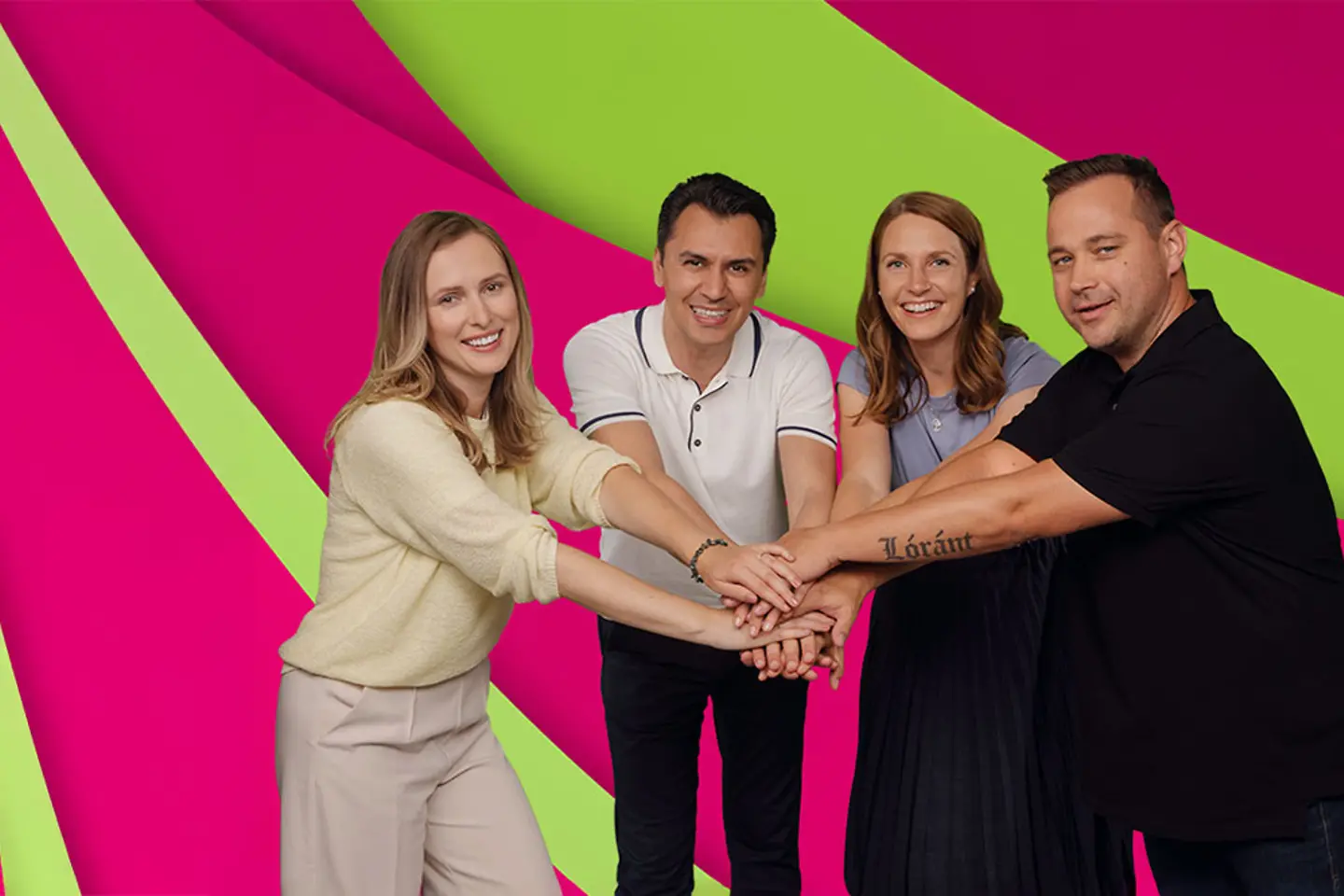 Four people stand next to each other, smile and put their hands on top of each other in the middle