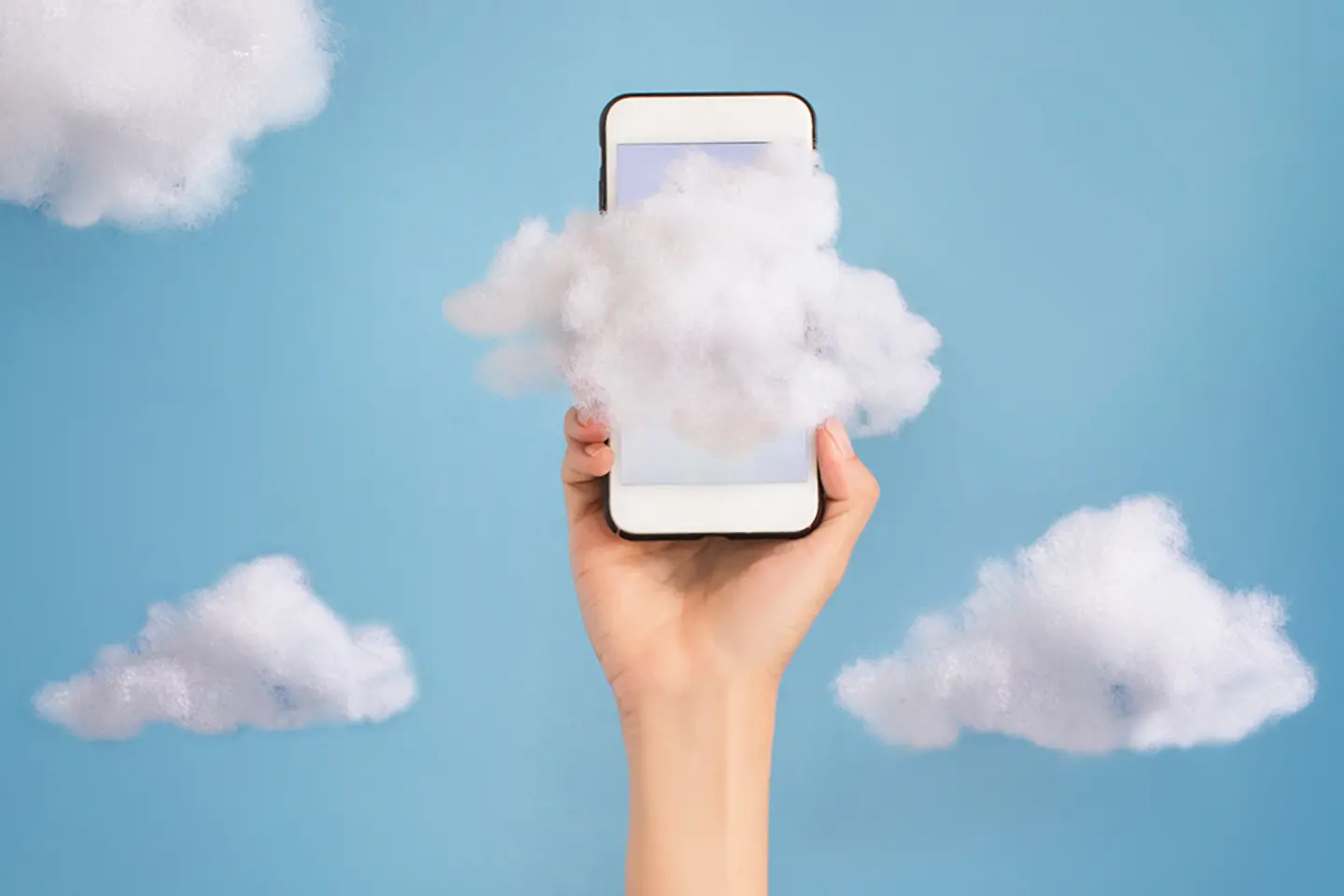 A hand holding a mobile phone high in the sky against a cloudy background