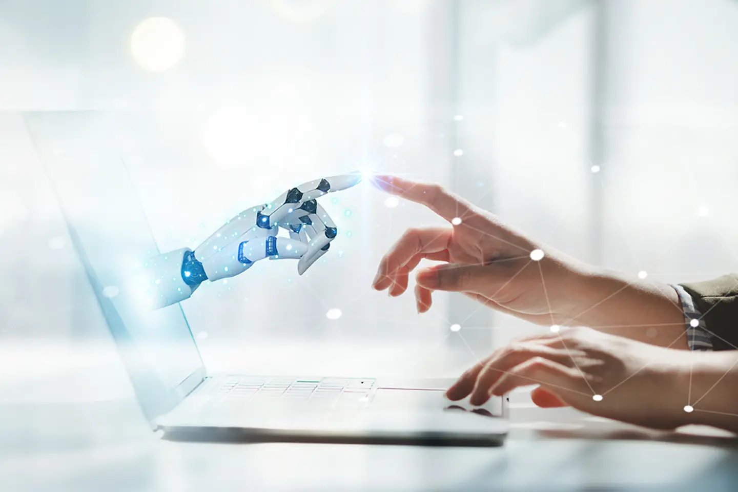 Human and robotic hands touching in front of a laptops display