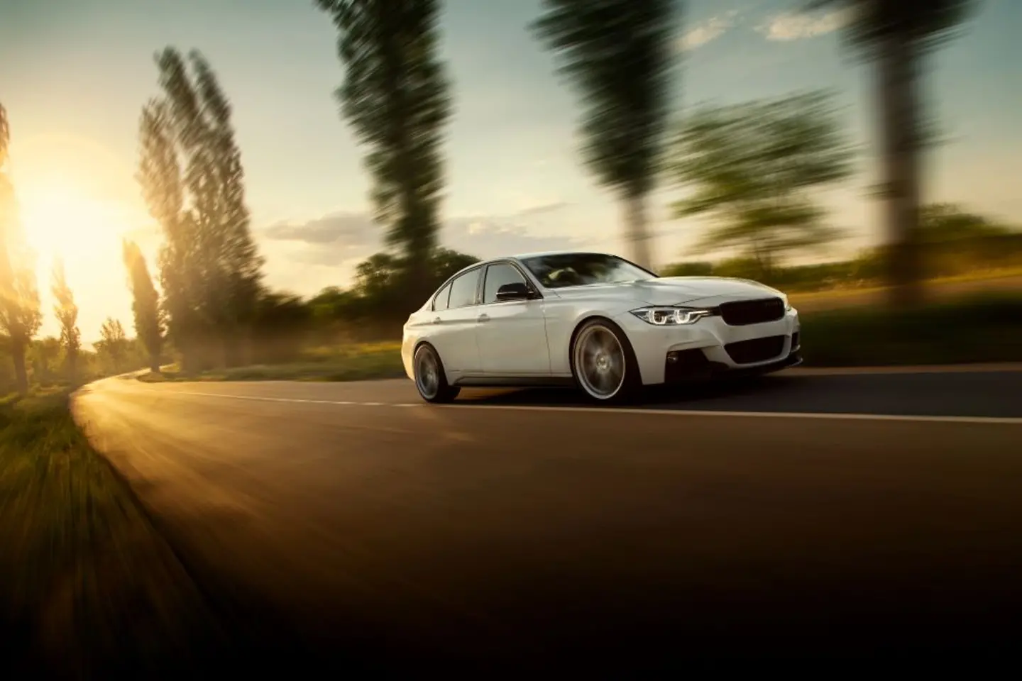 White car driving on a country road in the sunset