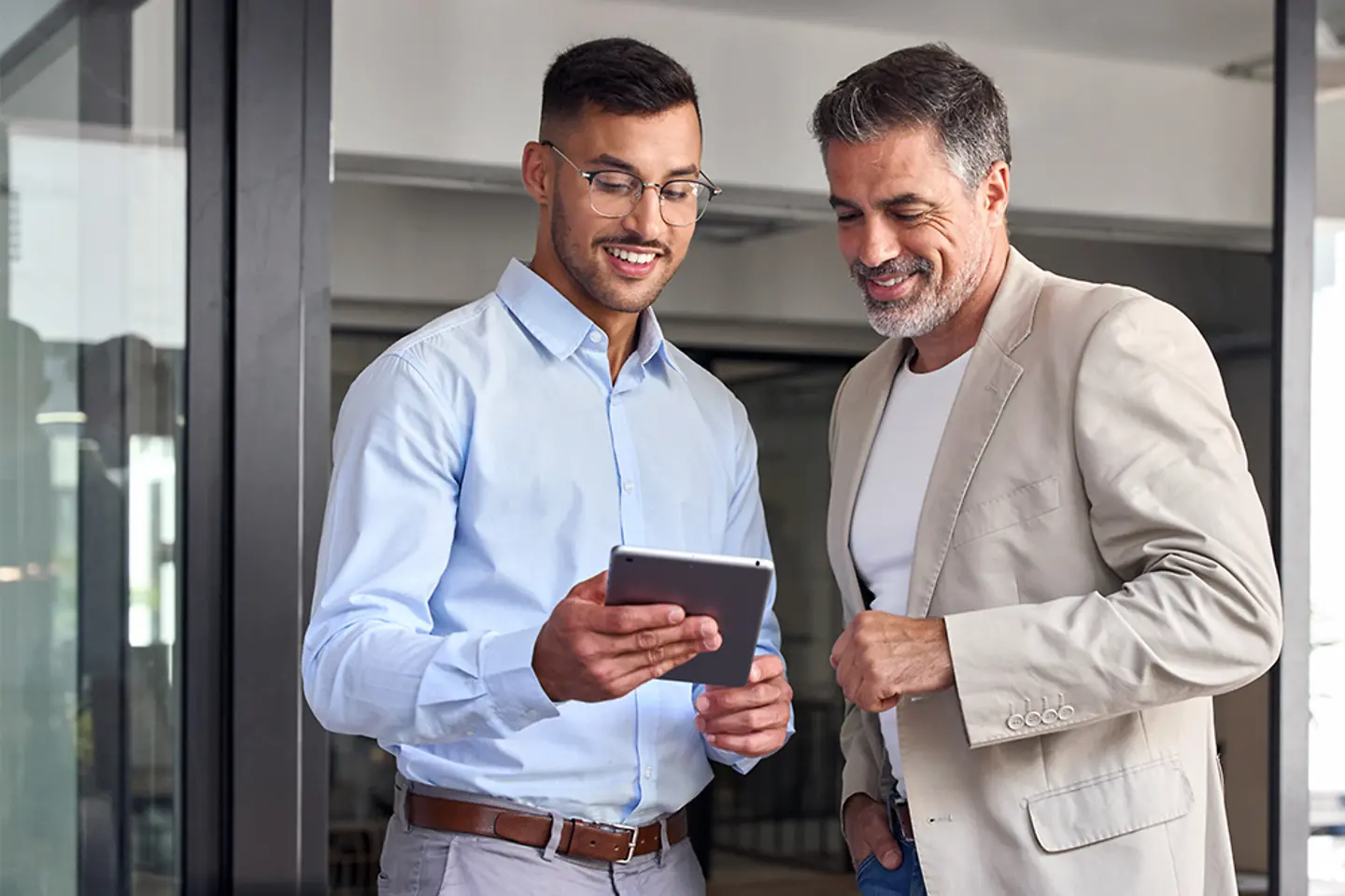 Dois empresários alegres trabalhando juntos em um escritório. Eles estão de pé e usando um tablet digital.