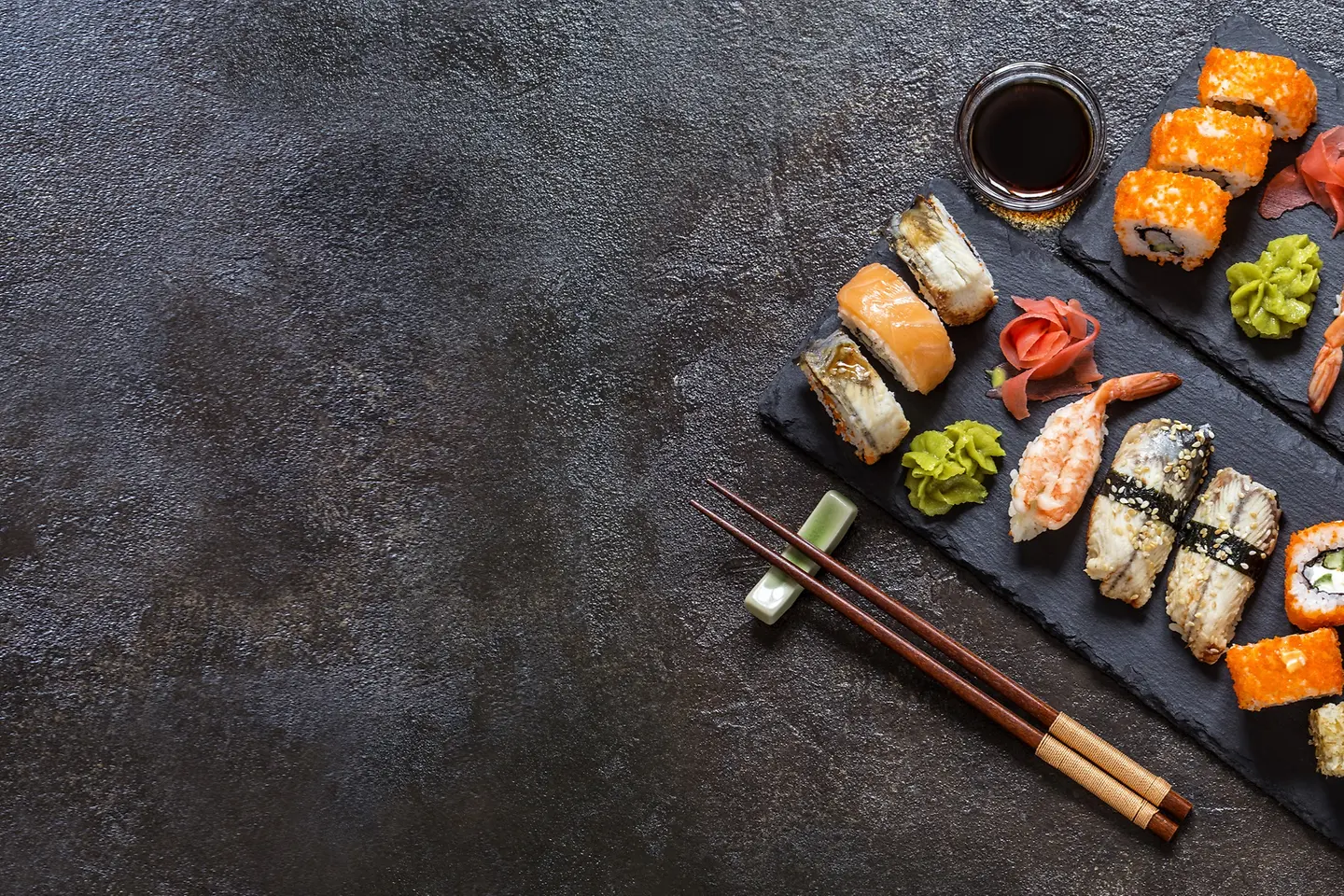 Sushi Rollen mit Reis, Fisch, Sojasauce auf einem dunklen steinernern Hintergrund