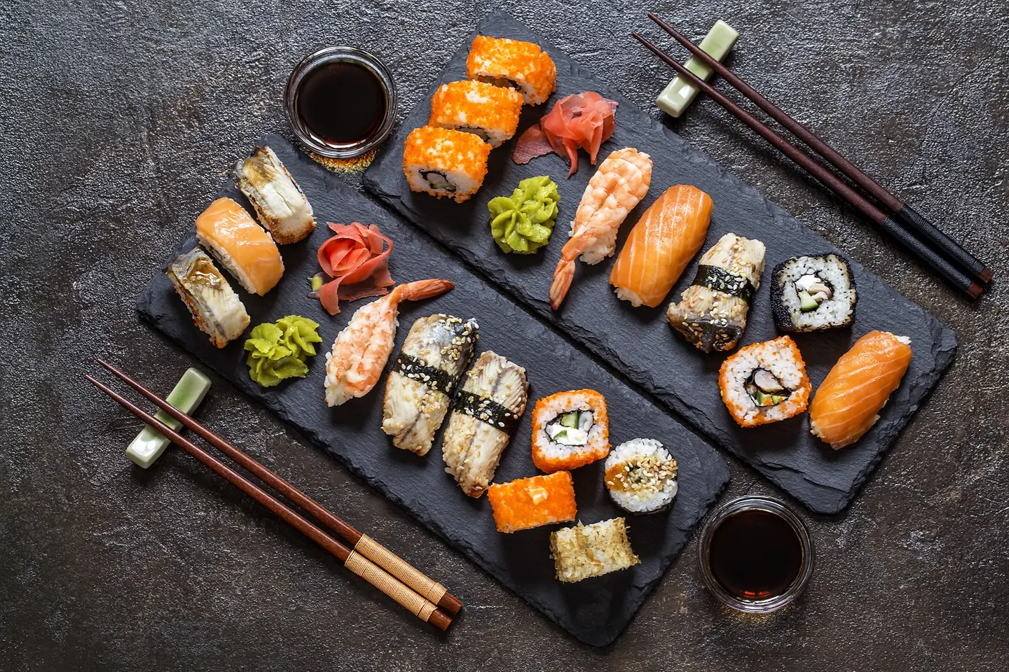 Sushi Rollen mit Reis, Fisch, Sojasauce auf einem dunklen steinernern Hintergrund