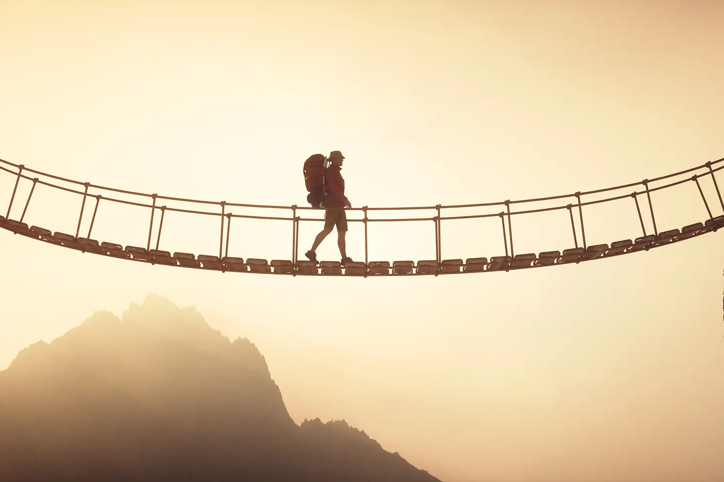 A hiker crossing a suspended bridge linking two mountain peaks
