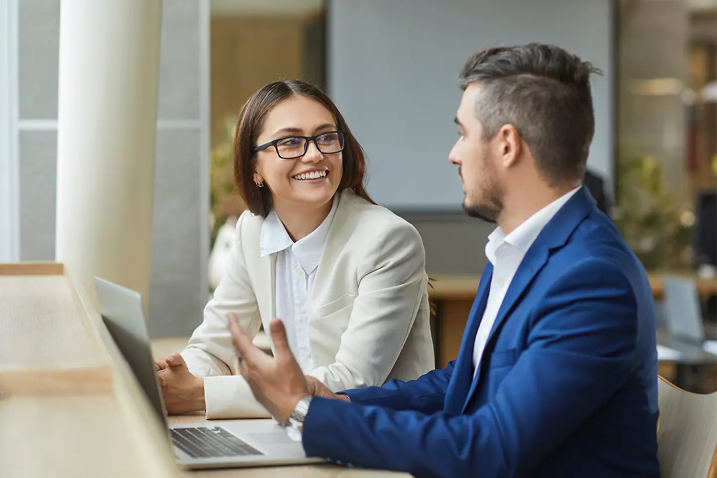 Deux jeunes employés souriants en conversation devant un ordinateur portable