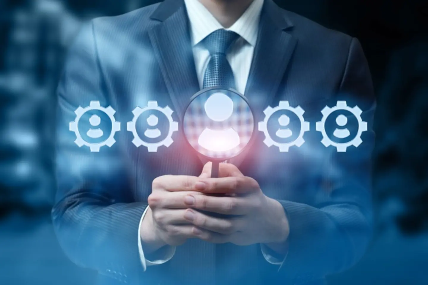 A businessman holds a magnifying glass, icons can be seen through and next to it.