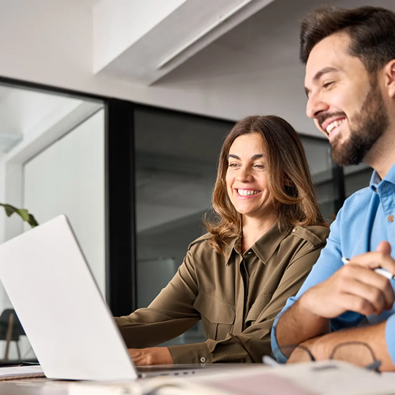 Two smiling professionals talking using laptop computer working in office